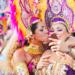 Two women Carnival dancers pose for a selfie as one kisses other on the cheek.