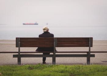 man sitting on brown bench facing on the sea