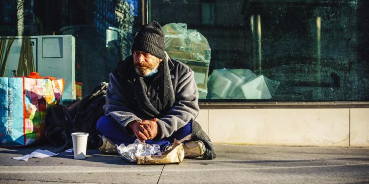 man in black and gray jacket sitting on sidewalk during daytime