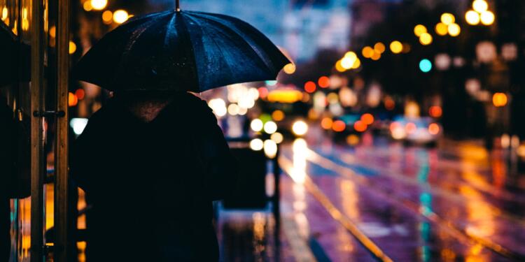 person walking on street while holding black umbrella near cars on road at nighttime