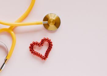 From above of yellow stethoscope near small red bead heart made for San Valentines Day on pale pink surface