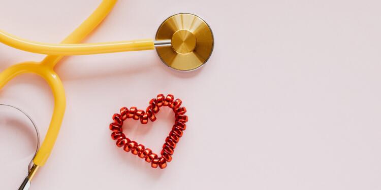 From above of yellow stethoscope near small red bead heart made for San Valentines Day on pale pink surface