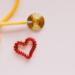 From above of yellow stethoscope near small red bead heart made for San Valentines Day on pale pink surface