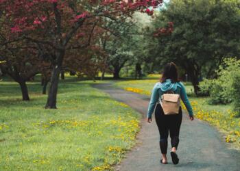 woman wearing blue jacket and black pants walking on grass field pathway