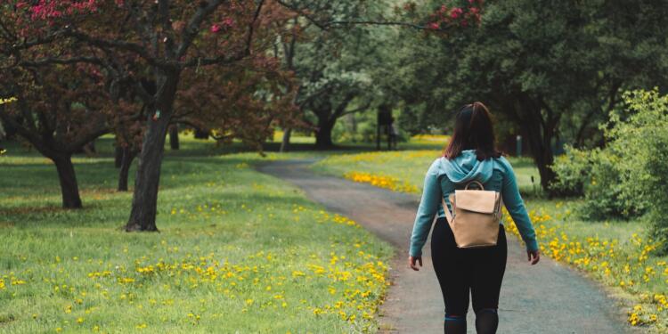 woman wearing blue jacket and black pants walking on grass field pathway
