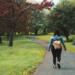 woman wearing blue jacket and black pants walking on grass field pathway