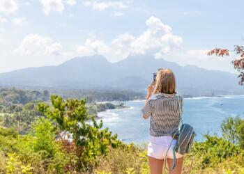a woman taking a picture of the ocean with her cell phone