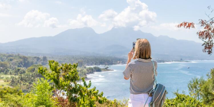 a woman taking a picture of the ocean with her cell phone